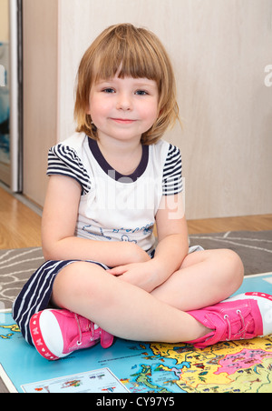 Diligent Russian girl sitting on the floor with big world children atlas book Stock Photo