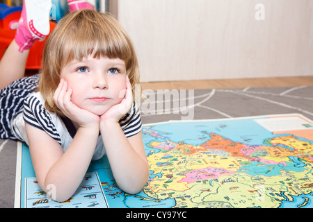 Diligent Russian girl laying on the floor with world children atlas book. Copyspace Stock Photo