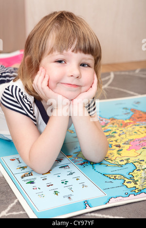 Smiling Russian girl laying on the floor with world children atlas book. Stock Photo