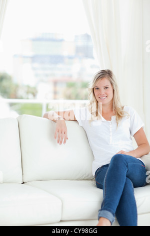 A woman with her arm resting on the couch as she sits and smiles Stock Photo