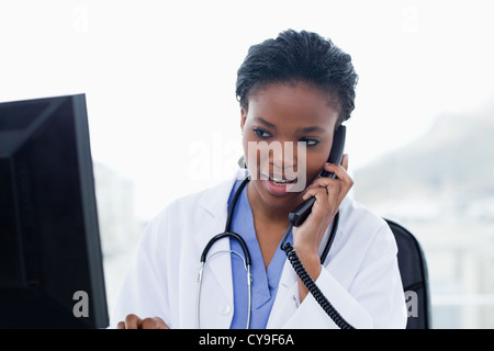 Female doctor on the phone while using a computer Stock Photo
