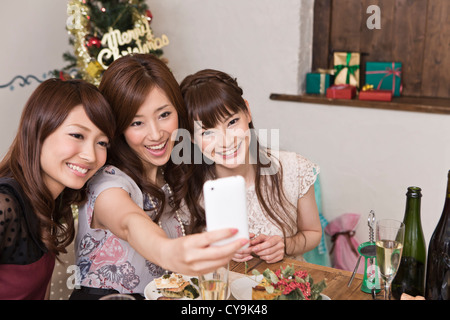 Three Young Women Taking Photograph with Smartphone at Christmas Party Stock Photo