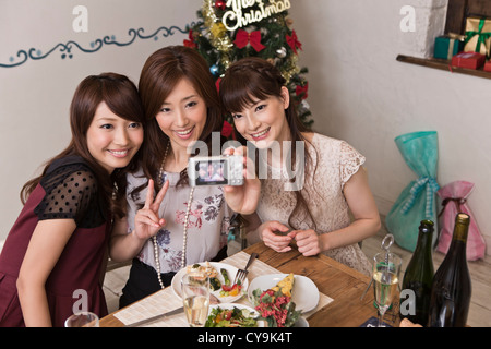 Three Young Women Taking Photograph with Digital Camera at Christmas Party Stock Photo