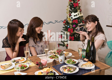 Three Young Women Taking Photograph with Instant Camera at Christmas Party Stock Photo