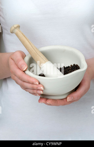 woman holding pestle and mortar with black peppercorns Stock Photo