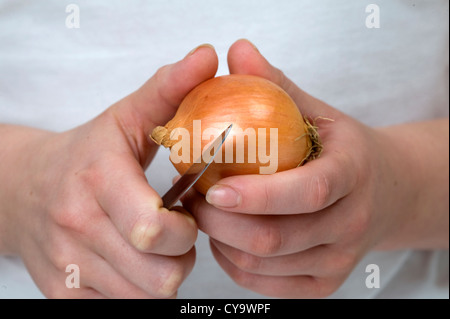 peeling an onion. woman using a knife to peel an onion held in her hands Stock Photo