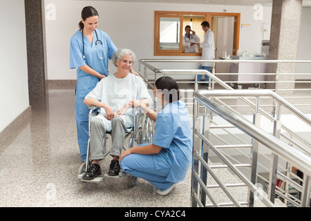 Two nurses talking with  old women sitting in wheelchair Stock Photo