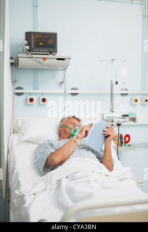 Man in oxygen mask reading in bed Stock Photo
