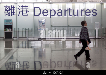 Elderly female walking to departures gate holding a bag, with liquid restrictions signs in background Stock Photo