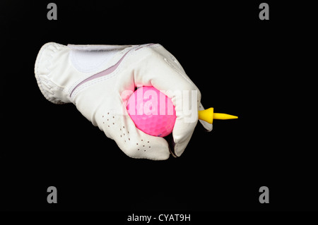 Hand in white golf glove holding pink golf ball and yellow tee peg all isolated on black background. Stock Photo