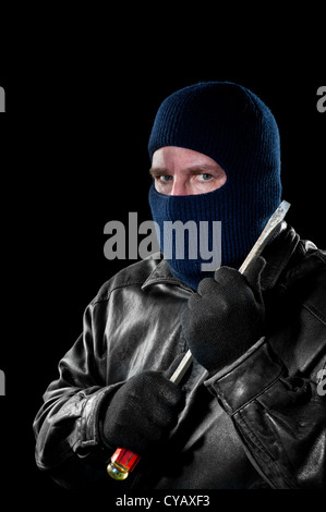 A criminal thief in a ski mask to hide his identity holds a large screwdriver as he prepared to commit a crime. Stock Photo