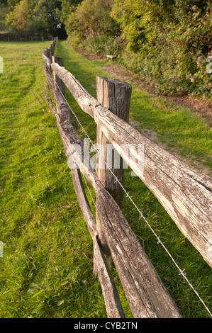 weathered wooden split rail fence besides footpath with barbed wire in between rails posts to keep in cattle livestock to field Stock Photo