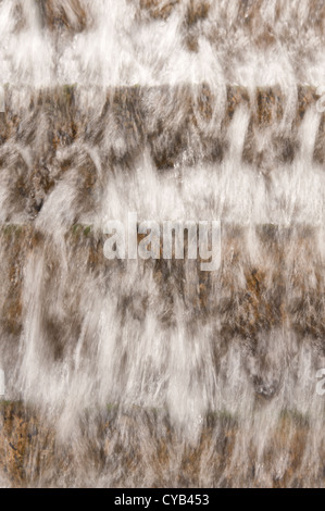 Waterfall and water stream in channel canal cutting flowing over stepped feature to land in pool Stock Photo