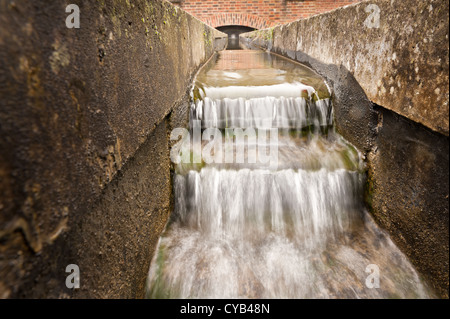 Waterfall and water stream in channel canal cutting flowing over stepped feature to land in pool Stock Photo