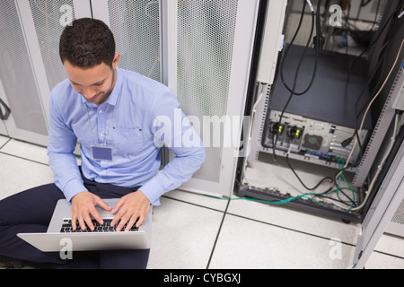 Technician typing on the laptop in front of server Stock Photo