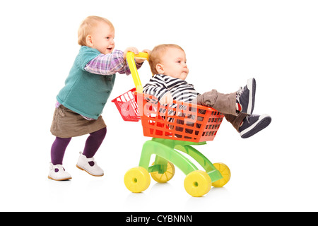 Toddler girl pushing her twin brother in a toy cart isolated on white background Stock Photo