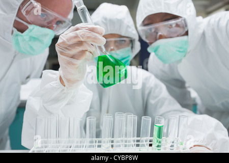 Chemist mixing green liquid in beaker with two chemists watching Stock Photo