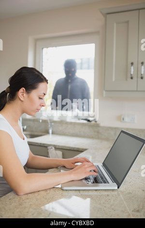 Woman using laptop with robber looking at her through window Stock Photo