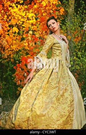 A pretty young woman in her late teens or early 20s in a beautiful fancy dress with colorful autumn trees Stock Photo