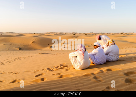 Men dressed in traditional Arab dress, sitting on a sand dune in a desert Stock Photo