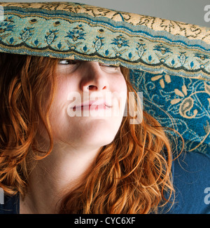 Portrait of young pretty woman in her 20's smiling and playing with a scarf which is partially covering her face Stock Photo