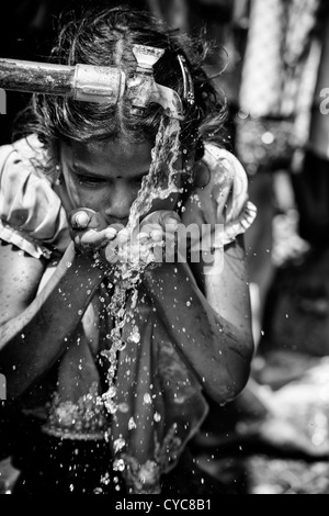 Indian girl drinking from a communal water tap in rural indian village. Andhra Pradesh, India. Black and white , selective focus. Stock Photo