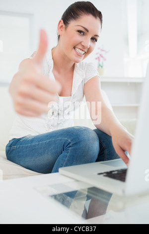 Woman using a laptop and giving thumbs up Stock Photo