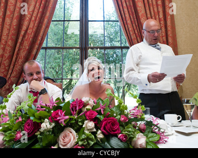 The bride and groom are amused during the father-of-the-bride's speech on their wedding day. Stock Photo