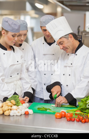 Chef teaching cutting vegetables to three trainees Stock Photo
