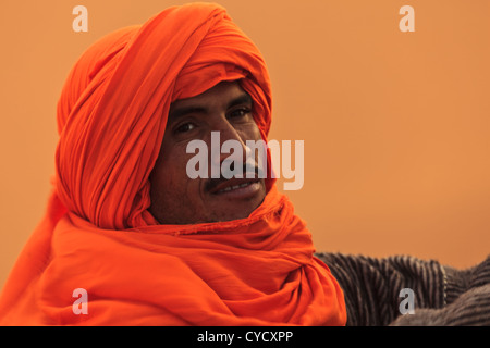 Portrait of Berber man in the Sahara with orange turban head garb blowing in the wind in Merzouga, Morocco. Stock Photo