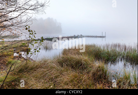 Small pier with boats on lake in cold still foggy morning Stock Photo