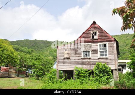 Blue sky white clouds view wooden house in green grass garden plot below green hill ridge, Windward, Carriacou, West Indies Stock Photo