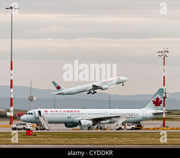 Air Canada jetliners at Vancouver International Airport. Boeing 777-300ER C-FIUR takes off Airbus A321-200 C-GJWO parked Stock Photo