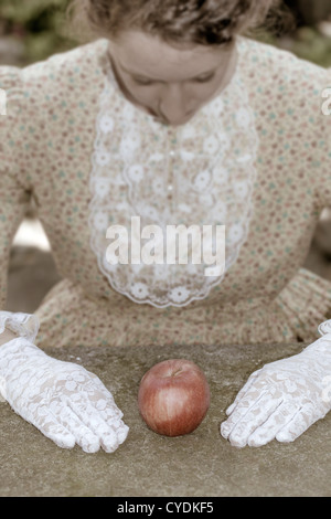 a woman in a victorian dress is sitting in front of an apple