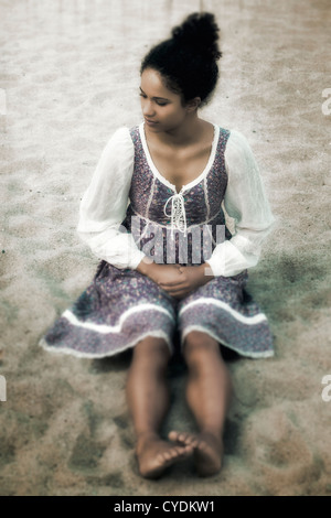 a young woman in a vintage dress sitting on the beach
