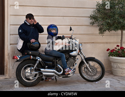 A young boy wearing a crash helmet astride his father's motorcycle, in Syracuse (Siracusa), Sicily, Italy Stock Photo