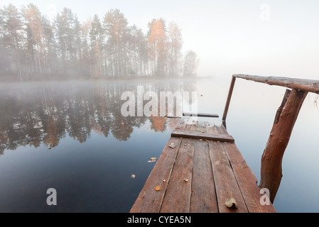 Small wooden pier on still lake in cold foggy morning Stock Photo