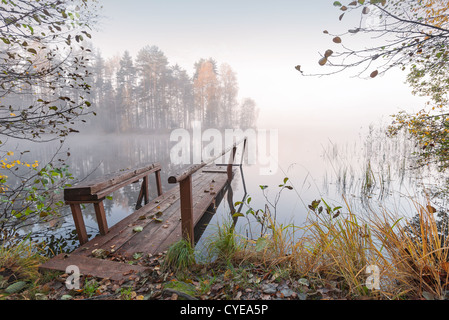 Small wooden pier on still lake in autumn foggy morning Stock Photo