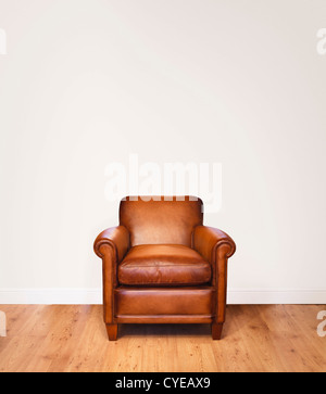 Leather armchair on a wooden floor against a white background with lots of space for copy.  The wall has a clipping path.