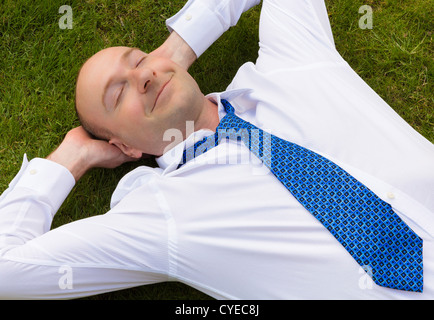 Businessman in shirt and tie relaxing on grass looking happy Stock Photo