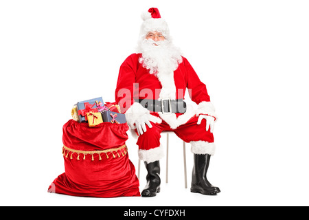 Santa Claus sitting with bag full of presents isolated on white background Stock Photo