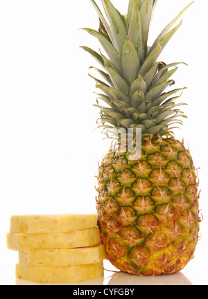 Fresh whole tropical pineapple with several slices stacked next to it on a white background Stock Photo