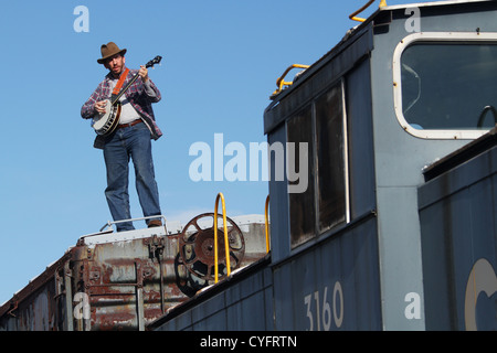 Male model as a hobo playing banjo while standing on a railroad box car. Stock Photo