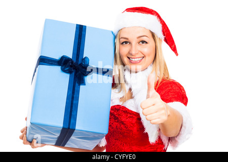 Young happy woman in Christmas Santa costume holding big blue gift box and gesturing thumb up, isolated on white background. Stock Photo