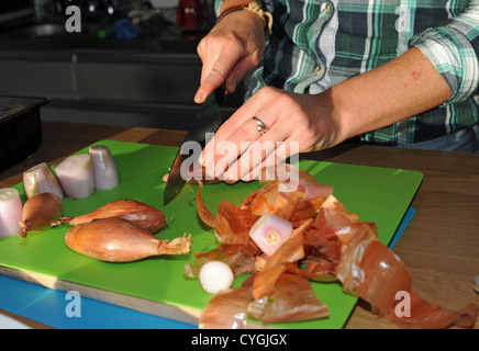 Cook chopping banana shallots on kitchen chopping board with sharp knife Stock Photo