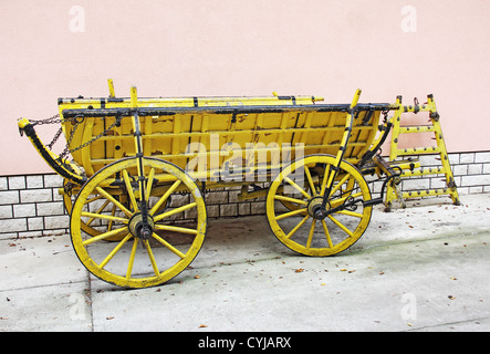 Old yellow wooden wagon standing in front of a wall of rose Stock Photo