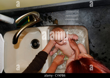 A six month old baby boy being bathed in the kitchen sink Stock Photo