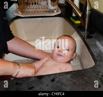 A six month old baby boy being bathed in the kitchen sink Stock Photo