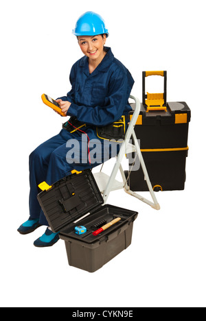 Builder woman sitting on step ladder and holding a voltage tester isolated on white background Stock Photo