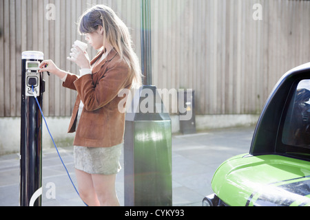 Woman charging electric car on street Stock Photo